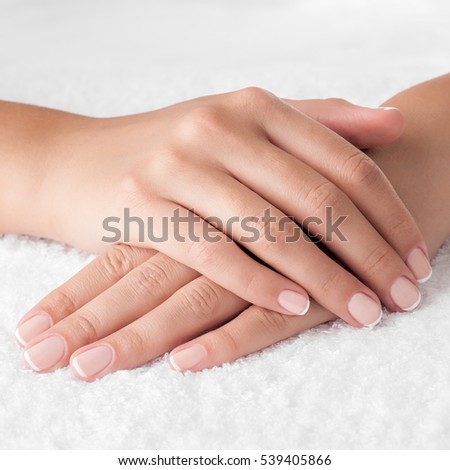 Beautiful french manicured woman hands on the white towel. Square composition.