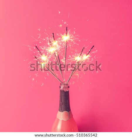 Champagne bottle with sparklers on pink background. Flat lay.
