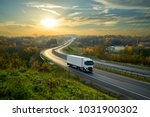 White truck driving on the highway winding through forested landscape in autumn colors at sunset