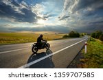 Motorcycle driving on the asphalt road in rural landscape at sunset with dramatic clouds                               