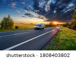 Motion blurred white fast delivery van driving on the asphalt road in rural landscape in the rays of the sunset with dark storm cloud