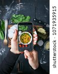 Small photo of Woman hands make smartphone photo of quinoa salad with vegetables - tomatoes, beans, greens - in white bowl on wooden board in dark style. Social networks phone photog. Vegan vegetarian healthy food