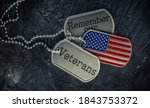 Small photo of US military soldier's dog tags engraved with Remember our Veteran's text and in the shape of the American flag. Memorial Day or Veterans Day concept.