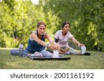 Small photo of Two mature woman stretching their legs after exercise in park. Beautiful athletic woman doing stretches in the park with her mixed race friend. Sporty mid adult lady stretching after workout session.