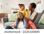 Cheerful little girl sitting on father shoulder while playing with mother at home. Happy black  family enjoying weekend at home. Cute little daughter sitting on fathers shoulder and play with her mom.