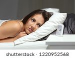 Small photo of Sleepless insomniac girl looking at alarm clock lying on a bed in the night at home