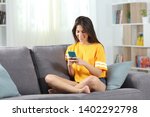 Full body portrait of a happy teen in yellow using phone sitting on a couch in the living room at home