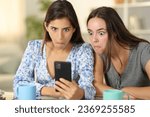 Small photo of Perplexed women cheking cell phone content sititng at home