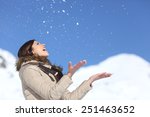 Happy woman throwing snow in the air on winter holidays with a snowy mountain and a blue sky in the background