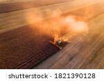 Harvesting oilseed rape in autumn field. Harvester combine in a cloud of dust glowing from the setting sun. Aerial top view