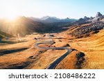 Fantastic aerial view on winding road in autumn mountain valley at sunset. The golden sunset light illuminates the mountains and orange grass. Passo Giau, Dolomite Alps, Dolomites, Italy