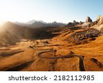 Picturesque aerial view on winding road in autumn mountain valley at sunset. The golden sunset light illuminates the mountains and orange grass. Passo Giau, Dolomite Alps, Dolomites, Italy