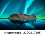 Aurora borealis Northern lights over famous Stokksnes mountains on Vestrahorn cape. Reflection in the clear water on the epic skies background, Iceland. Landscape photography