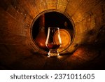 A glass of scotch whiskey in old oak barrel. Copper alambic and small barrel on background. Traditional alcohol distillery concept