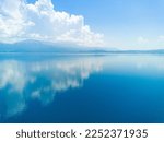 Majestic huge white thick clouds float across the clear blue daytime sky above the horizon with the shallow azure calm Adriatic Sea in the light of the bright summer sun