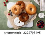 Small photo of Homemade freshly baked bagels on a parchment paper ready to eat, cinnamon raisin, sesame and plain bagel served with cream cheese and fresh berries