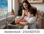 Small photo of Little boy rinsing fruits under tap water under control on his mother