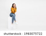 Portrait of excited screaming young asian woman sitting on white box isolated over white background, Wow and surprised concept