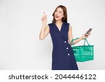 Beautiful Asian woman holding shopping basket and mobile phone on hand and pointing empty blank space in side isolated on white background, Shopping online concept