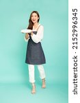 Small photo of Young Asian woman housewife wearing kitchen apron cooking and holding empty white plate or dish isolated on green background, Full length composition