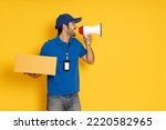 Happy delivery man with a package and name tag speaking into a mega phone isolated on yellow background