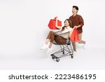 Small photo of Asian woman sitting inside of shopping trolley and holding shopping bag and Asian man pushing shopping cart isolated on white background