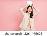 Small photo of Happy Asian woman holding white piggy bank isolated on pink background, Saving money and financial economize concept