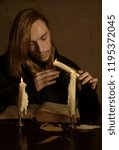 Small photo of long-haired man thought about something after breaking away from reading an old book and dripping his hand with wax from a candle