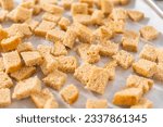 Baking croutons seasoned with olive oil and spiced on a baking sheet lined with parchment paper.