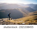 Small photo of A female hiker descending a rocky path towards Sail from Crag Hill with the summits of High Snockrigg and Robinson in winter in the English Lake District, UK.