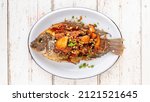 Small photo of tasty large fried nile tilapia fish with garlic and chili in oval ceramic plate on white wooden texture background, top view, flat lay, light and airy food photography