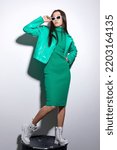 Small photo of Fashion asian female model. Green total look. Green leather jacket, green dress, white boots, sunglasses. Asian fashion