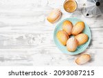 Small photo of Perfect French madeleine cookies, buttery and delicate, powdered with icing sugar served with cup of coffee. White wooden background. Top view