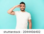 Young arab man isolated on blue background saluting with hand with happy expression