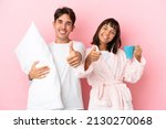 Young couple in pajamas isolated on pink background giving a thumbs up gesture because something good has happened