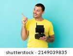 Brazilian man holding a drone remote control over isolated blue background intending to realizes the solution while lifting a finger up