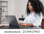 Black businesswoman typing on laptop, looking at the screen. Office room with shelf on blurred background. Concept of distance work and manager