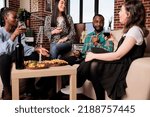 Small photo of Multiethnic group of cheerful people drinking alcoholic beverages while chatting at birthday event. Smiling heartily young adults having wine party at home while celebrating friendship anniversary.