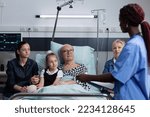Small photo of African american female nurse filling out recovery report of sick man bedridden in geriatric hospital. Family listening grandfather health status updates. Doctor writing elderly medical record.