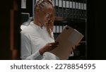 Small photo of Private investigator analyzing gathered information in police agency office. Woman detective sitting in evidence room and reading archive records, studying clues and case files.