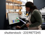African american worker looking at inventory report on computer, working at merchandise quality control in storehouse. Stockroom supervisor preparing customers orders for shipping in warehouse