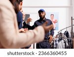 African American man security guard in uniform controlling entrance of fashion store, talking with anxious shoppers wait in line for Black Friday sales. Crowd control during holiday shopping season
