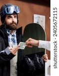 Small photo of Detailed view of male snowboarder tipping employee with cash in ski hotel reception. Caucasian man in wintersport clothing giving gratuity to concierge at winter mountain resort.