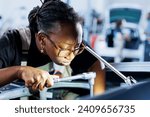 African american engineer does client car maintenance in auto repair shop using lamp light after vehicle shut down unexpectedly. Trained expert in garage mending customer damaged automobile fuel tank