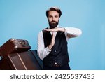 Small photo of Hotel porter shows timeout symbol on camera, asking for a break working in hospitality and travel industry. Classy doorman in suit and tie indicating pause sign with hands, professional job.