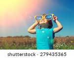 Happy little girl with big sunglasses walking in the meadow and looking at the sun