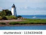 Sailboat passing by tower of Black Rock Harbor lighthouse, also referred to as Fayerweather Island light, near the rocky shoreline of Seaside Park, on a warm summer day in Bridgeport, Connecticut.