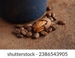 Small photo of ENAMEL MUG ON RUSTED SURFACE WITH SME COFFEE BEANS SPILT NEXT TO A PARTIALLY SHELLED PECAN NUT