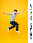 Energetic excited young Asian man in casual clothes jumping studio shot isolated in colorful yellow background