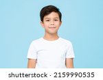 Cute smiling boy in plain white t shirt looking at camera in isolated studio light blue color background
